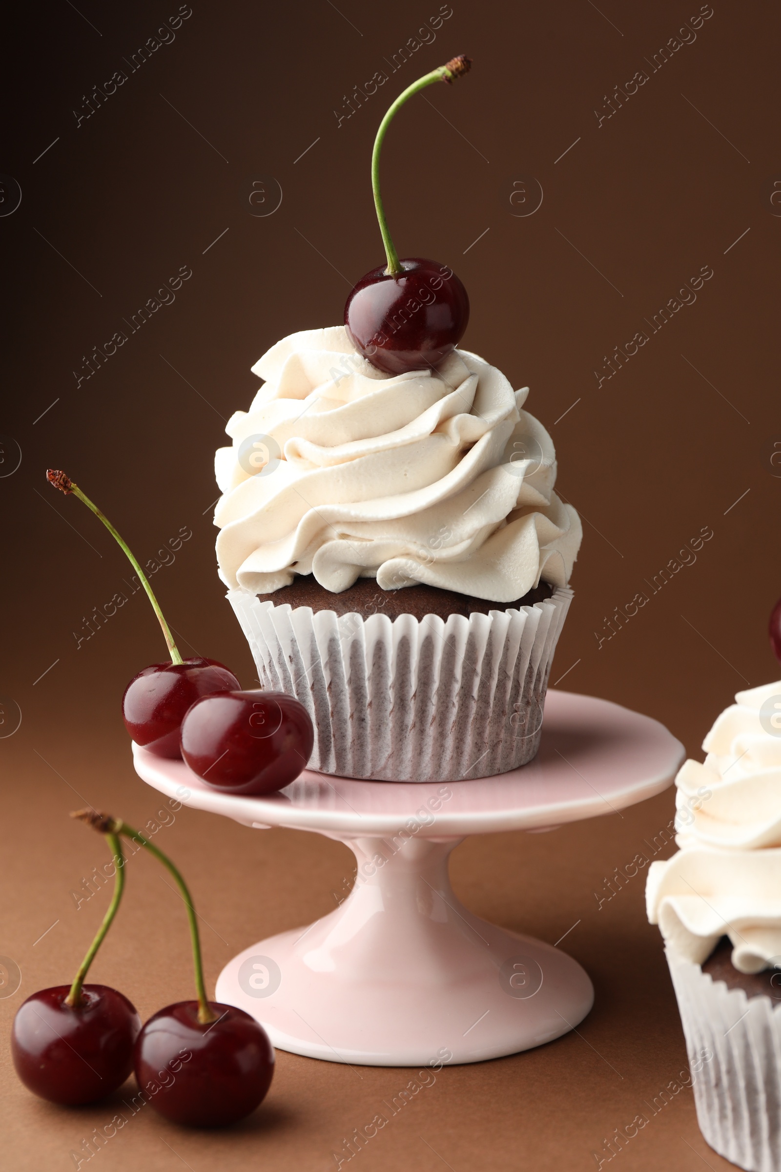 Photo of Delicious cupcakes with cream and cherries on brown background