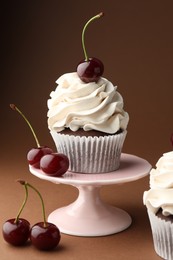 Delicious cupcakes with cream and cherries on brown background