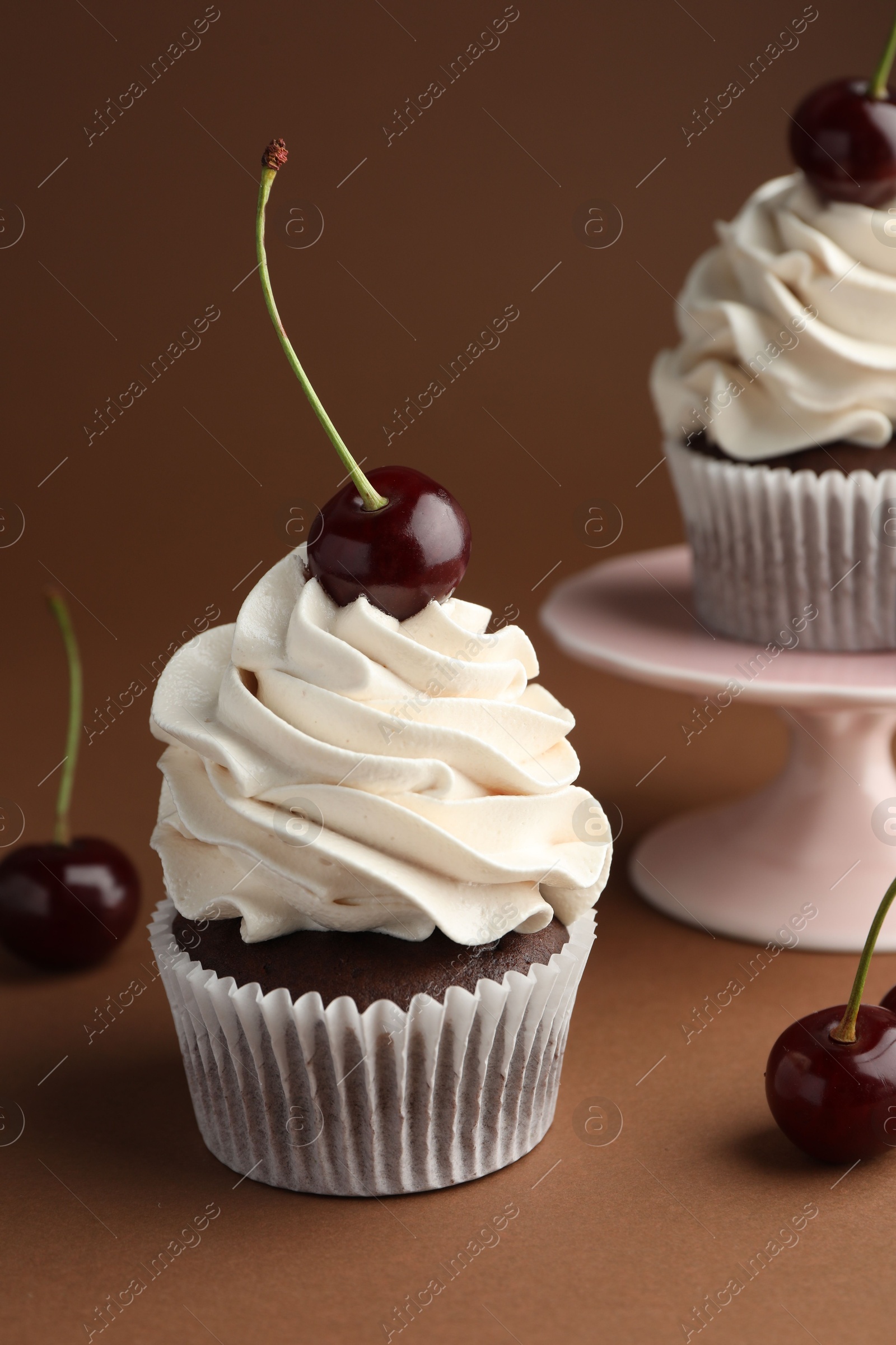 Photo of Delicious cupcakes with cream and cherries on brown background