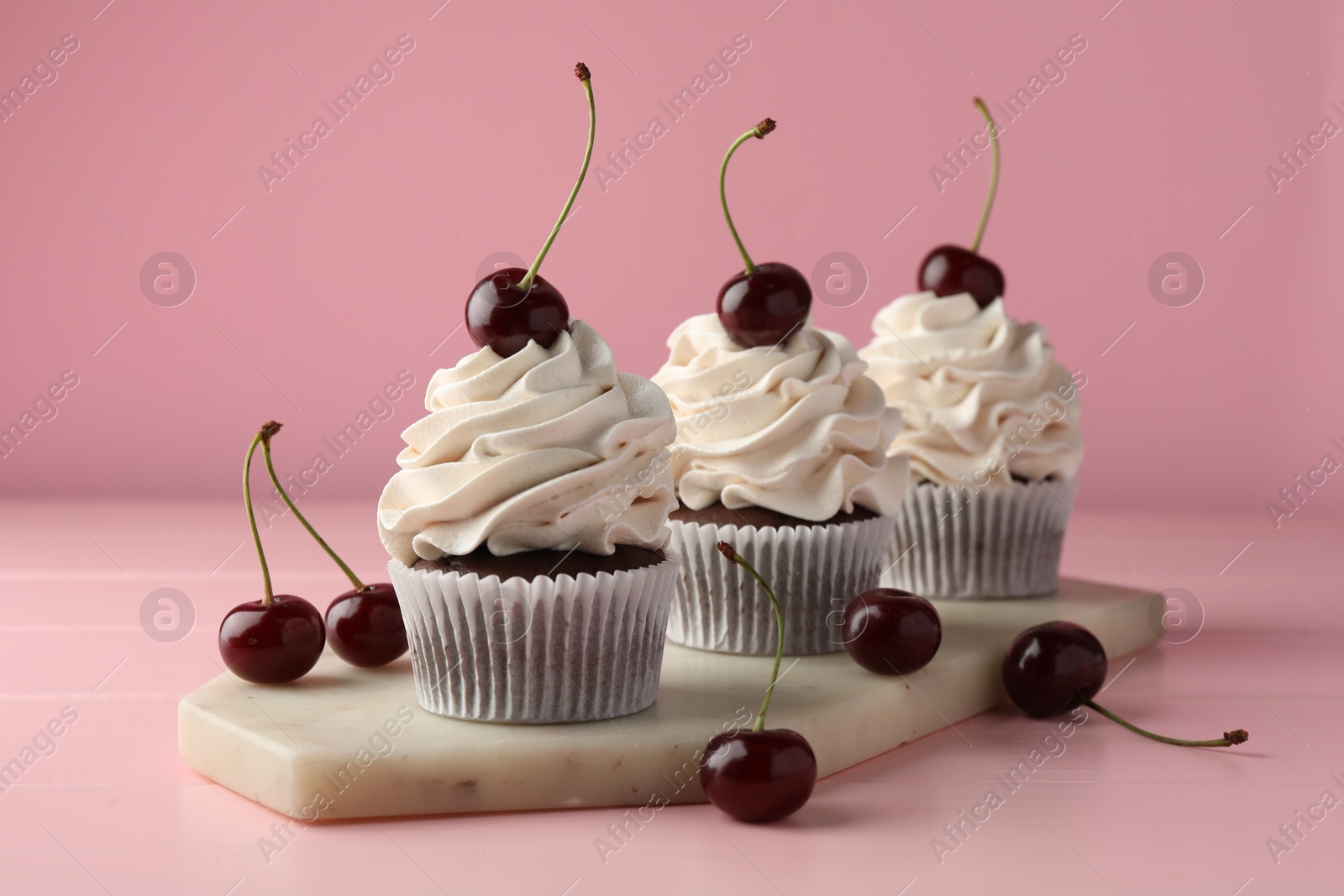 Photo of Delicious cupcakes with cream and cherries on pink table