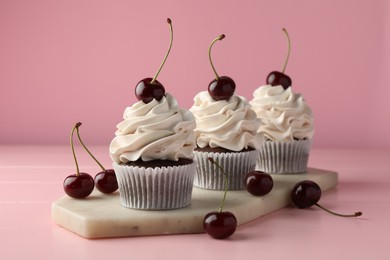 Photo of Delicious cupcakes with cream and cherries on pink table