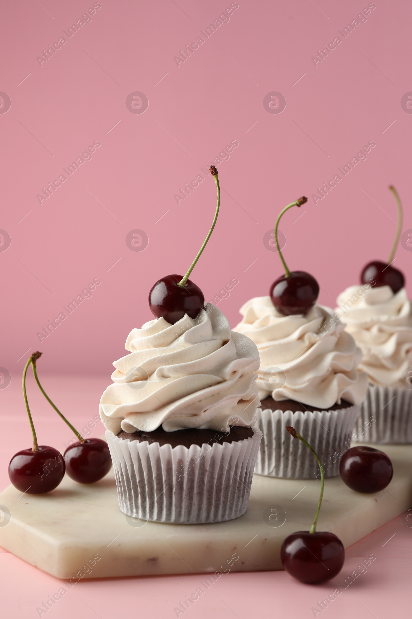 Photo of Delicious cupcakes with cream and cherries on pink table