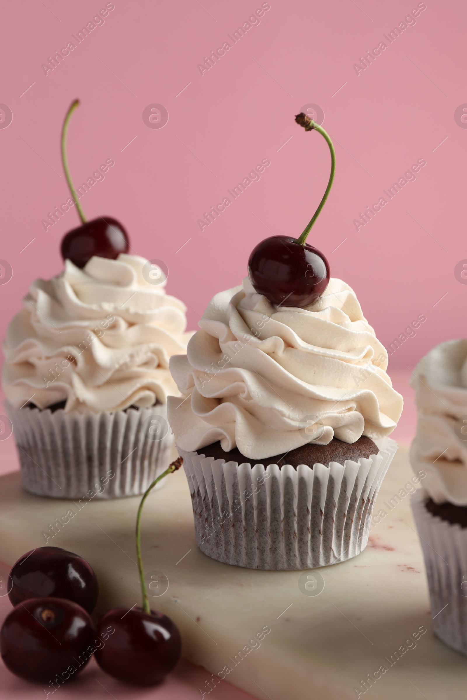 Photo of Delicious cupcakes with cream and cherries on pink background