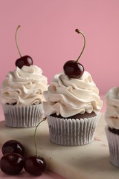 Delicious cupcakes with cream and cherries on pink background