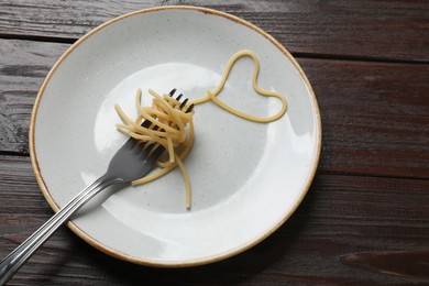 Heart made of tasty spaghetti and fork on wooden table. Space for text