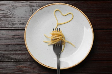 Heart made of tasty spaghetti and fork on wooden table, top view