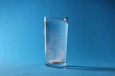Effervescent pill dissolving in glass of water on light blue background