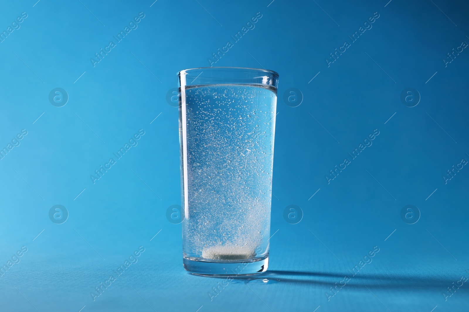 Photo of Effervescent pill dissolving in glass of water on light blue background