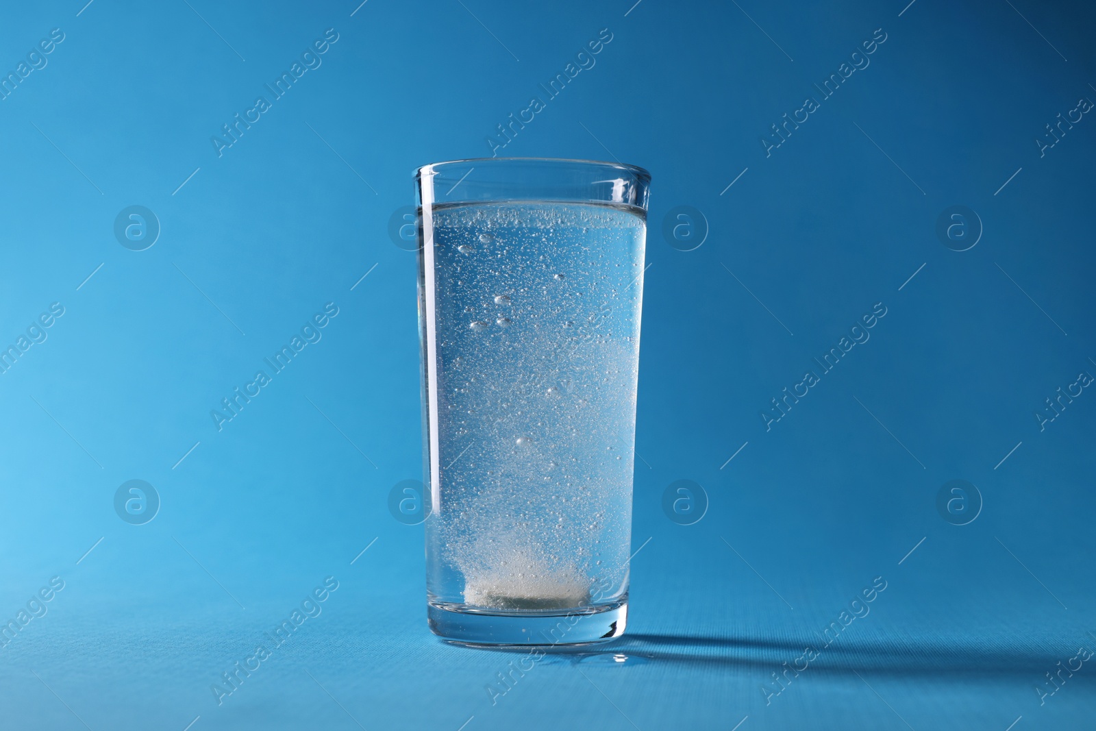 Photo of Effervescent pill dissolving in glass of water on light blue background