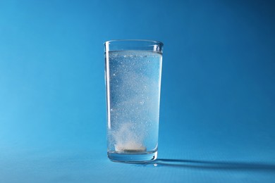 Effervescent pill dissolving in glass of water on light blue background