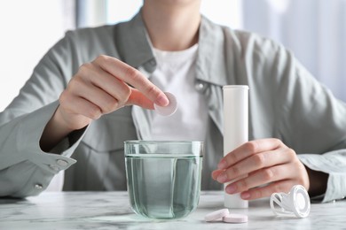 Woman putting effervescent pill into glass of water at white marble table, closeup