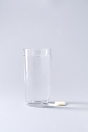 Photo of Effervescent pill and glass of water on light grey background
