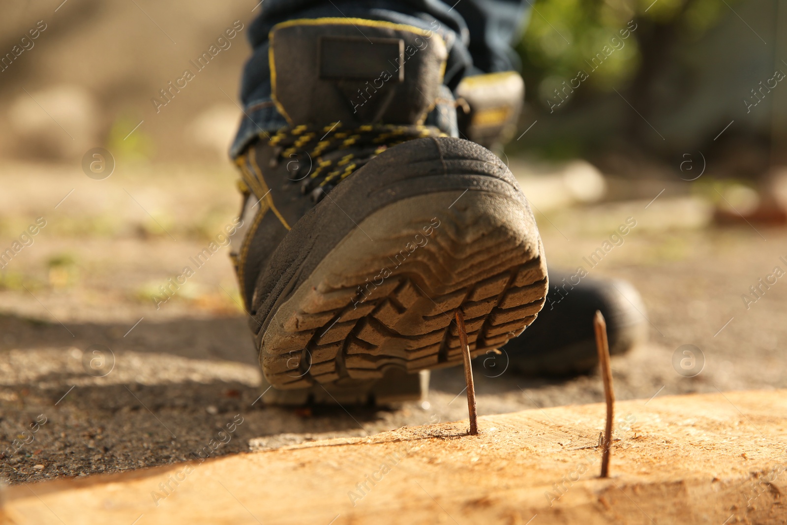 Photo of Careless worker stepping on nail in wooden plank outdoors, closeup