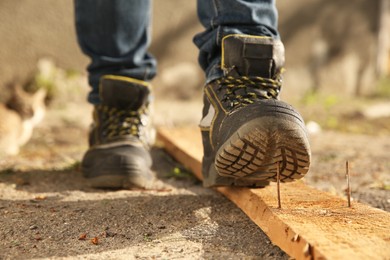 Careless worker stepping on nail in wooden plank outdoors, closeup