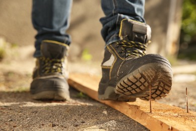 Photo of Careless worker stepping on nail in wooden plank outdoors, closeup