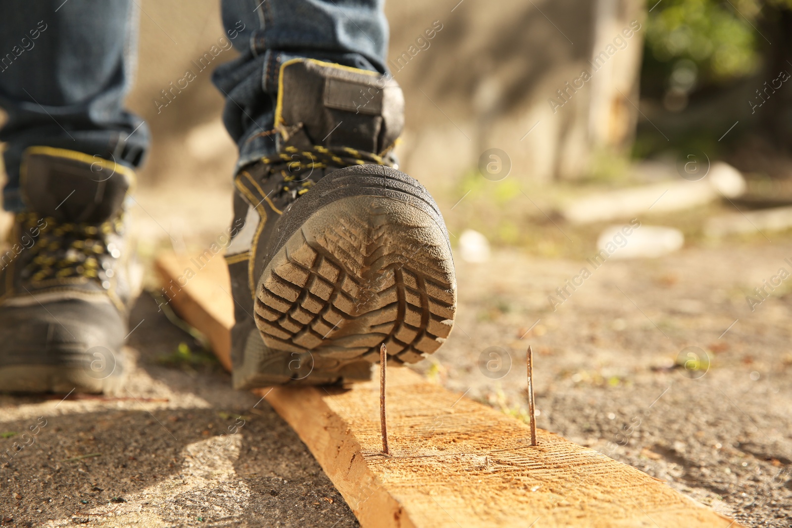 Photo of Careless worker stepping on nail in wooden plank outdoors, closeup