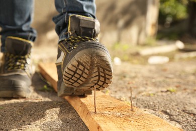 Careless worker stepping on nail in wooden plank outdoors, closeup