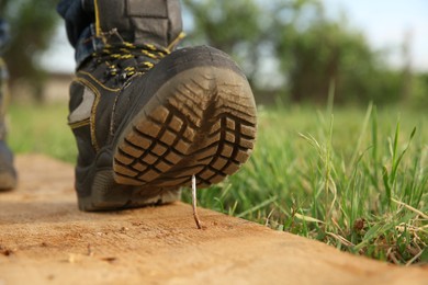 Photo of Careless worker stepping on nail in wooden plank outdoors, closeup