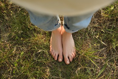 Photo of Woman standing barefoot on green grass outdoors, top view