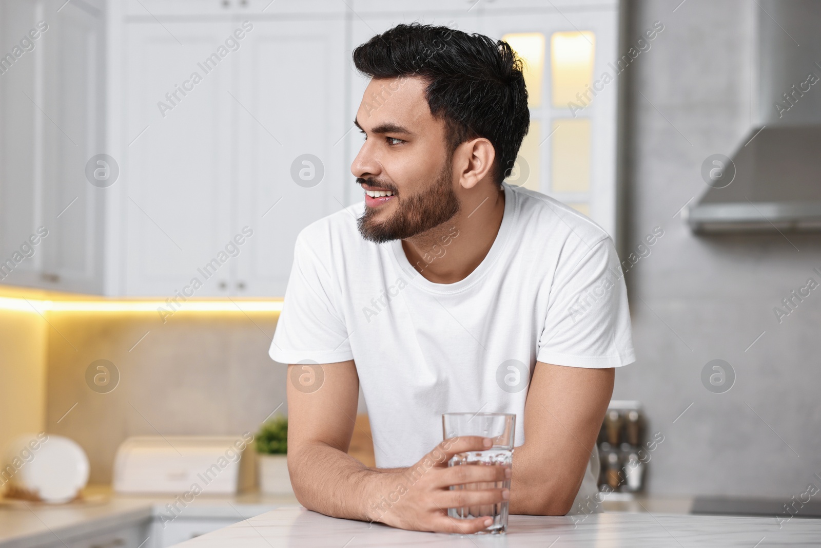 Photo of Happy man with glass of water at table in kitchen at morning