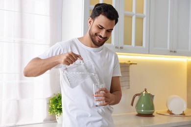 Photo of Morning of happy man pouring water from jug into glass in kitchen