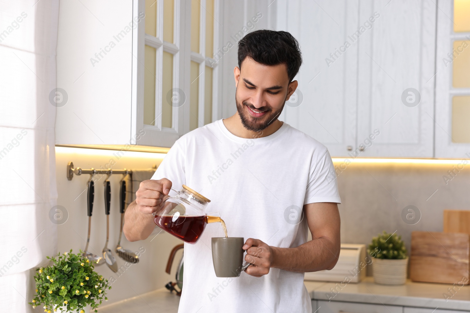 Photo of Morning of happy man pouring coffee from teapot into cup in kitchen