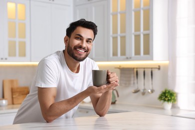 Morning of happy man with cup of hot drink at table in kitchen. Space for text