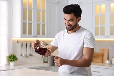 Morning of happy man pouring coffee from teapot into cup in kitchen