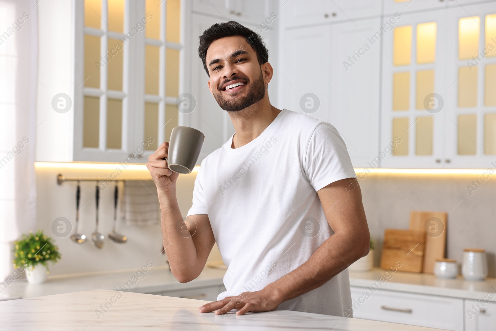 Photo of Morning of happy man with cup of hot drink at table in kitchen