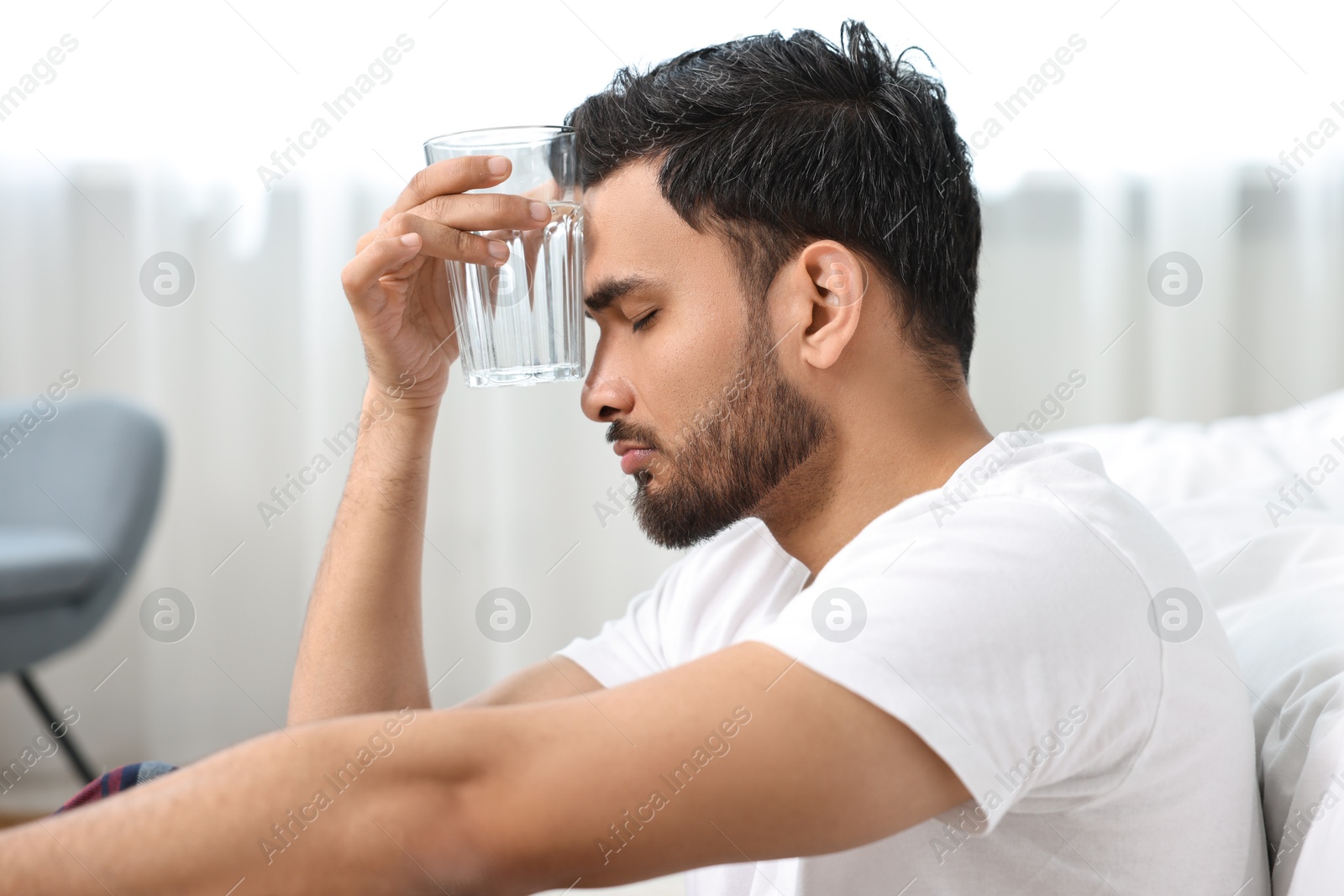 Photo of Man suffering from headache with glass of water at morning