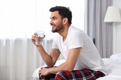 Happy man with glass of water on bed at morning