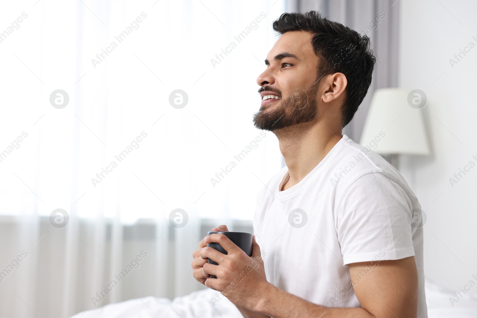Photo of Happy man with cup of morning coffee at home. Space for text