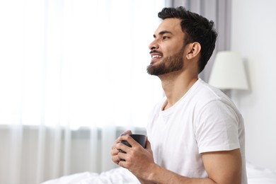 Happy man with cup of morning coffee at home. Space for text