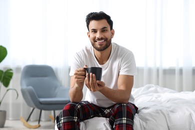 Happy man with cup of coffee on bed at morning