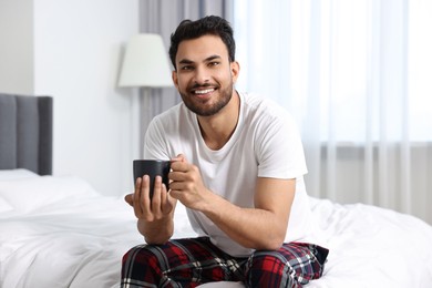 Photo of Happy man with cup of coffee on bed at morning