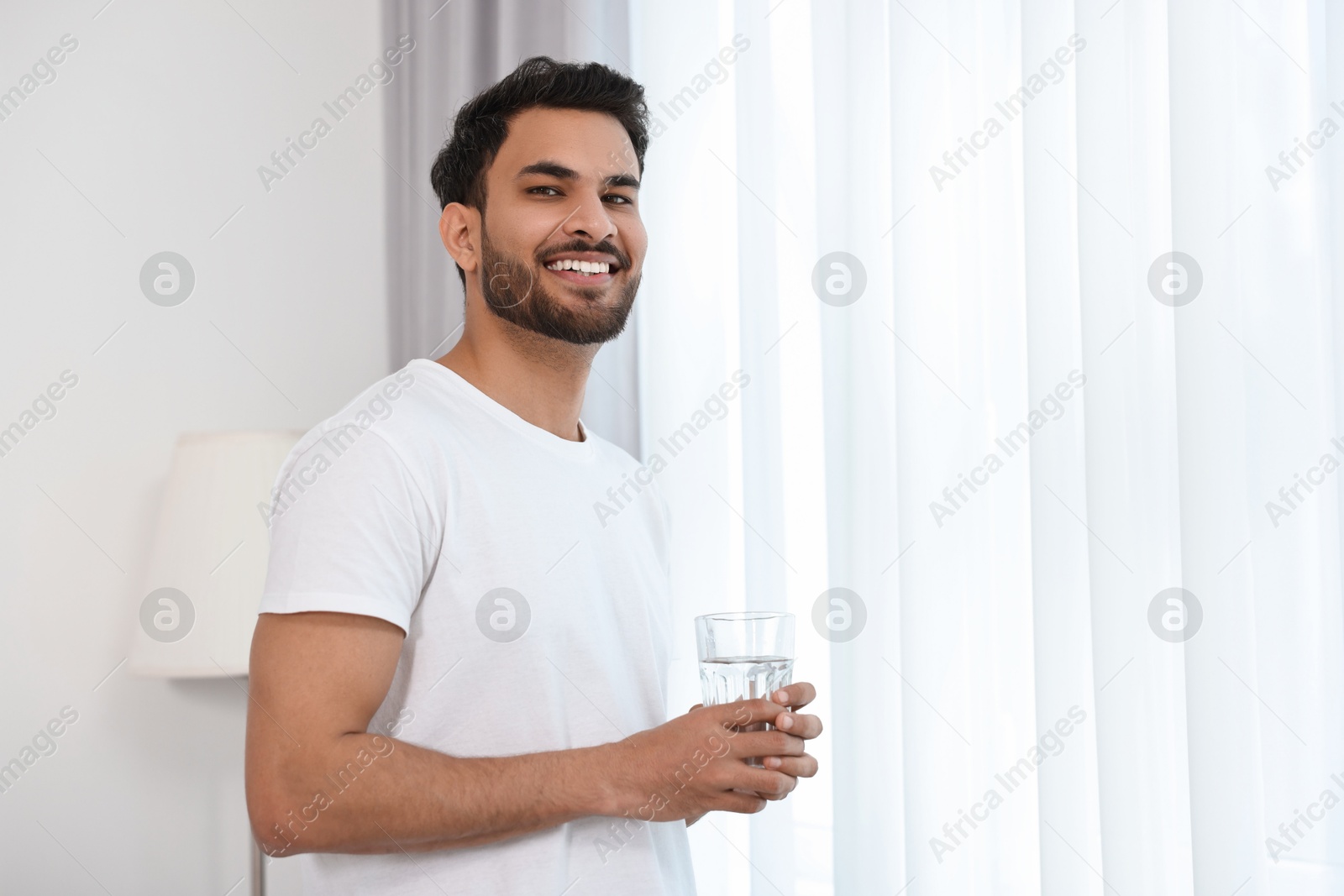 Photo of Happy man with glass of water at morning. Space for text