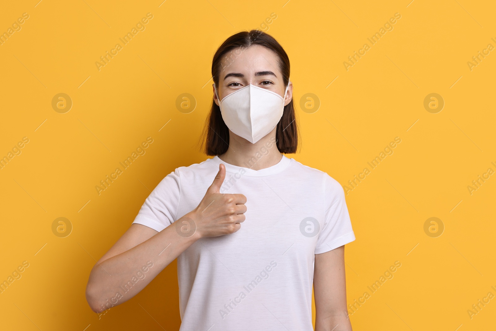 Photo of Woman in respirator mask showing thumbs up on orange background