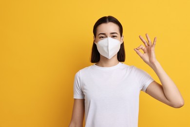 Photo of Woman in respirator mask showing OK gesture on orange background, space for text