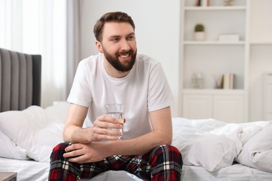 Photo of Happy man with glass of water on bed at morning