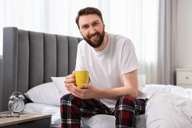 Happy young man with cup of coffee on bed at morning