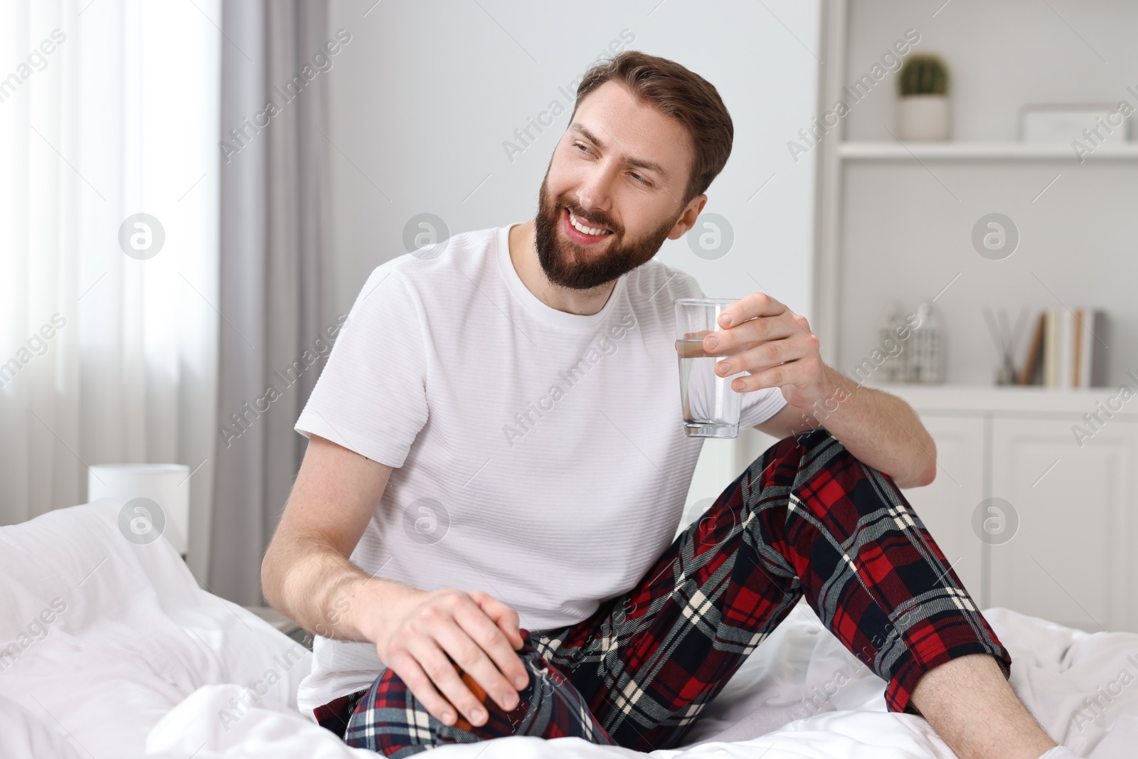 Photo of Happy young man with glass of water near on bed at morning