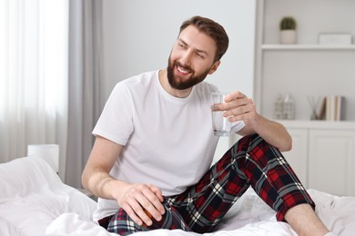 Happy young man with glass of water near on bed at morning