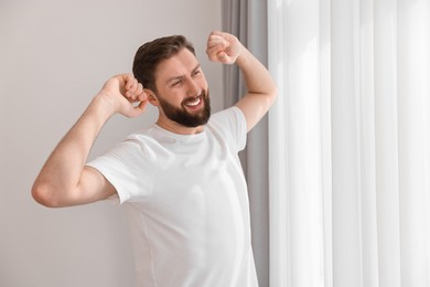 Happy young man stretching near window at morning