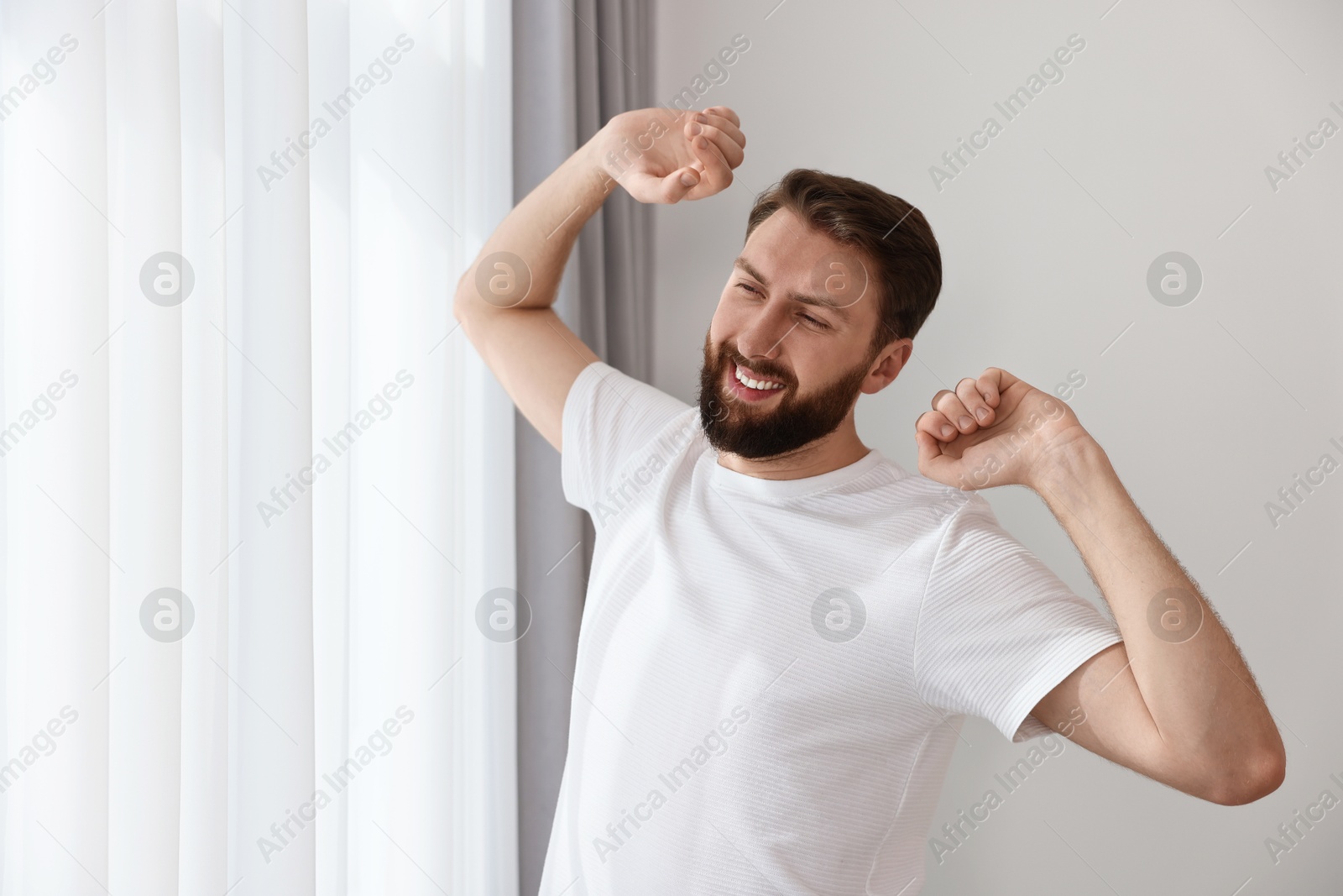 Photo of Happy young man stretching near window at morning