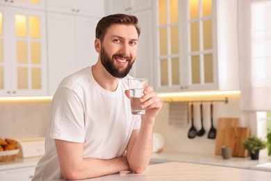 Photo of Happy young man with glass of water in kitchen at morning