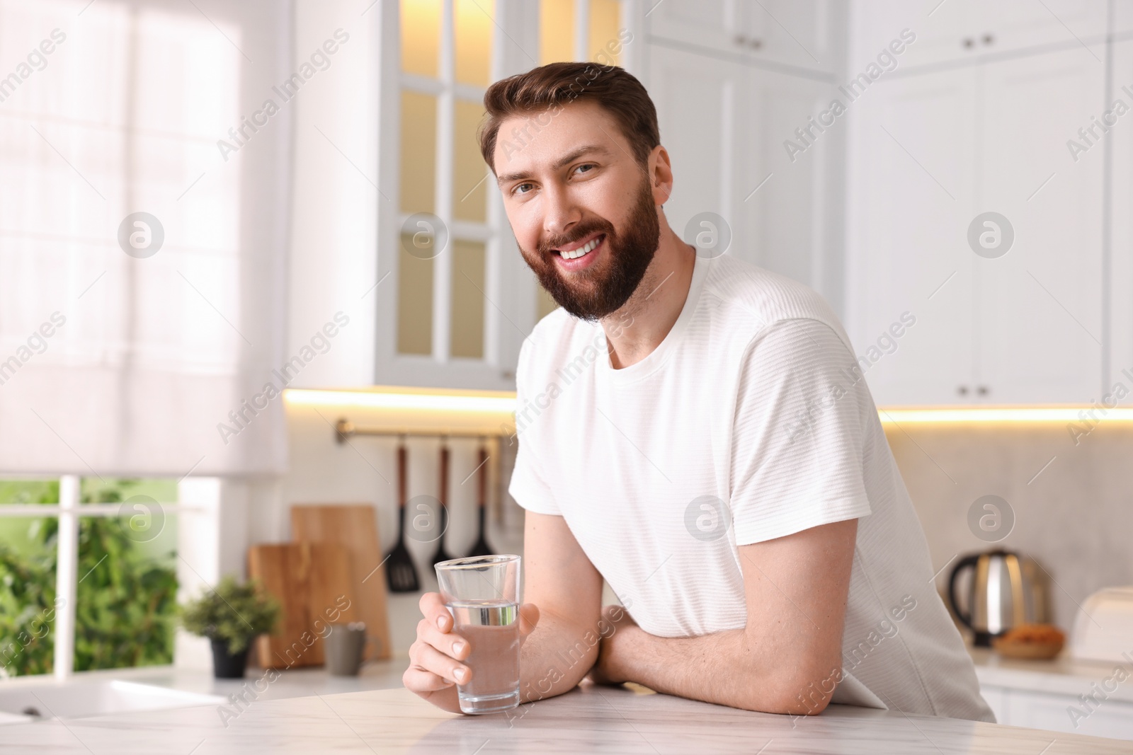 Photo of Happy young man with glass of water in kitchen at morning