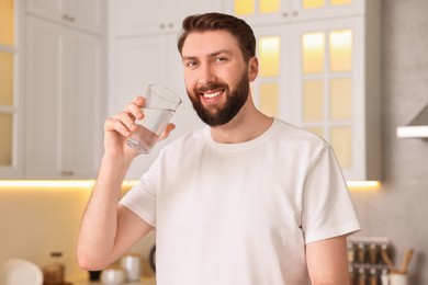 Happy young man with glass of water in kitchen at morning