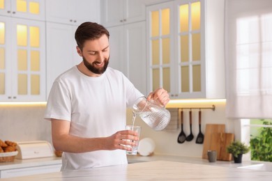 Happy young man pouring water into glass in kitchen at morning