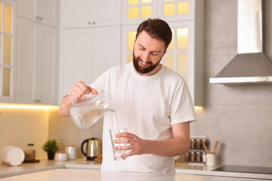 Happy young man pouring water into glass in kitchen at morning