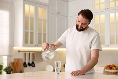 Happy young man pouring water into glass in kitchen at morning